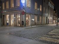 a very pretty light and brick street by some buildings by night time with a person walking on the sidewalk