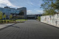 a city street surrounded by grass and tall buildings at the end of a street there is a paved pathway in front of the building