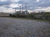 a group of power plants with buildings in the background and gravel ground in foreground