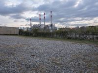 a group of power plants with buildings in the background and gravel ground in foreground