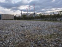 a group of power plants with buildings in the background and gravel ground in foreground
