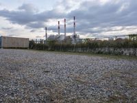a group of power plants with buildings in the background and gravel ground in foreground