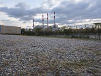 a group of power plants with buildings in the background and gravel ground in foreground