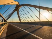 a bridge with sunlight casting shadows on the road and bridge posts and bridge cables on top