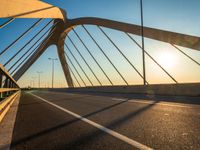 a bridge with sunlight casting shadows on the road and bridge posts and bridge cables on top