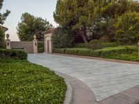 the gate to the private home is located behind a garden of shrubs and trees with concrete pillars