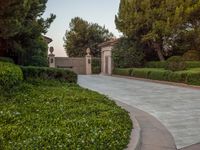 the gate to the private home is located behind a garden of shrubs and trees with concrete pillars