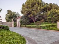 the gate to the private home is located behind a garden of shrubs and trees with concrete pillars