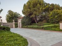 the gate to the private home is located behind a garden of shrubs and trees with concrete pillars