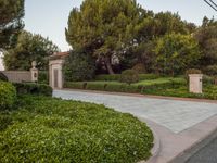 the gate to the private home is located behind a garden of shrubs and trees with concrete pillars