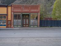 a red fire hydrant sitting in front of an old store window and building next to an open air field