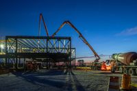 a picture of a building being built on a field near a forest in the background