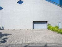 a brick walkway with an open garage door, grass, and bushes in front of it