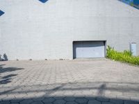 a brick walkway with an open garage door, grass, and bushes in front of it