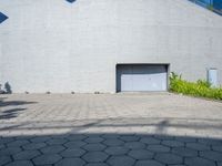 a brick walkway with an open garage door, grass, and bushes in front of it