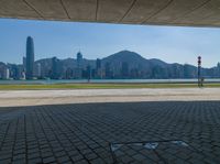 an empty park is on the edge of a large bay near buildings and water with green lawning