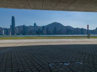 an empty park is on the edge of a large bay near buildings and water with green lawning