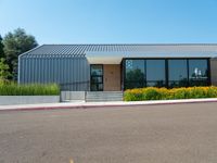 a metal and glass building with large windows in front of it and a parking space near the curb