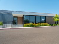 a business building with a parking lot, bushes and stairs on one side, a sidewalk and grass growing on the other side