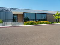 a business building with a parking lot, bushes and stairs on one side, a sidewalk and grass growing on the other side