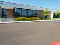 a business building with a parking lot, bushes and stairs on one side, a sidewalk and grass growing on the other side