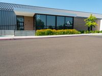 a business building with a parking lot, bushes and stairs on one side, a sidewalk and grass growing on the other side