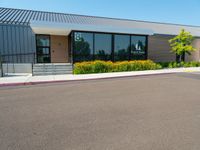 a business building with a parking lot, bushes and stairs on one side, a sidewalk and grass growing on the other side