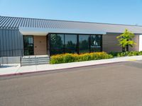 a business building with a parking lot, bushes and stairs on one side, a sidewalk and grass growing on the other side