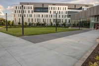 a city street surrounded by grass and tall buildings at the end of a street there is a paved pathway in front of the building