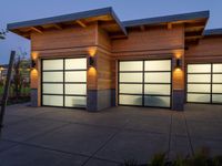 three garage doors are lit by outside lamps on a concrete patio next to trees and grass