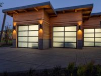 three garage doors are lit by outside lamps on a concrete patio next to trees and grass