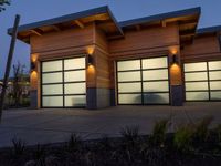 three garage doors are lit by outside lamps on a concrete patio next to trees and grass