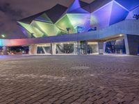 an illuminated up building surrounded by stone pavement and lights on in the distance is people