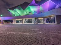 an illuminated up building surrounded by stone pavement and lights on in the distance is people