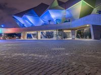 an illuminated up building surrounded by stone pavement and lights on in the distance is people