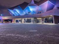 an illuminated up building surrounded by stone pavement and lights on in the distance is people