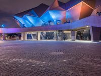 an illuminated up building surrounded by stone pavement and lights on in the distance is people