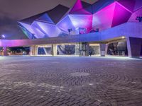 an illuminated up building surrounded by stone pavement and lights on in the distance is people