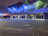 an illuminated up building surrounded by stone pavement and lights on in the distance is people