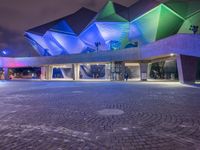 an illuminated up building surrounded by stone pavement and lights on in the distance is people