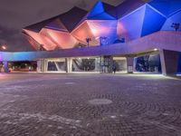 an illuminated up building surrounded by stone pavement and lights on in the distance is people