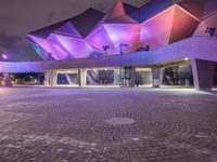 an illuminated up building surrounded by stone pavement and lights on in the distance is people