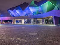 an illuminated up building surrounded by stone pavement and lights on in the distance is people