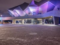 an illuminated up building surrounded by stone pavement and lights on in the distance is people