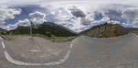 a panoramic image of an empty road with mountains in the background and clouds