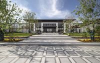 the large courtyard has several tables and chairs near the walkway leading to a building that has multiple windows on the front of it