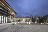 large gravel courtyard with lighted lights and architecture on the side of it, surrounded by trees