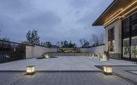 a courtyard with benches in a park by the water on a cloudy evening with some trees