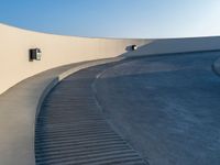 an empty white wall with a long curved walkway near it on the outside of a building