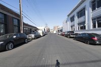 the shadow of a person riding a bike down a quiet street with many parked cars